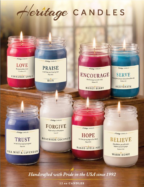 Eight Heritage Candles in glass jars on a wooden table, each labeled with an inspirational word (Love, Praise, Encourage, Serve, Trust, Forgive, Hope, Believe).